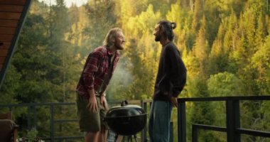 İki arkadaş, kozalaklı ormana tepeden bakan bir piknikte duygusal olarak iletişim kurup gülüyorlar. Izgarada yemek pişirirken iletişim.