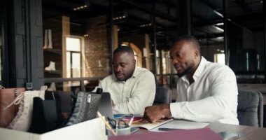 2 Black-skinned businessmen in white shirts are sitting in an office at a shoe factory and discussing a new shoe color. Managers have a color palette on which they consider possible colors for the