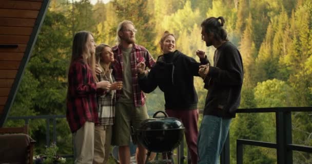 野餐时的气氛很温暖 那家伙弹吉他 他的朋友们跳舞 在以高山和针叶林为背景的烤架上做饭时的娱乐 — 图库视频影像