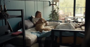 Sarışın kız köpeğiyle yatağa uzanıp onu okşadı. Evcil hayvanınla barış ve uyum.