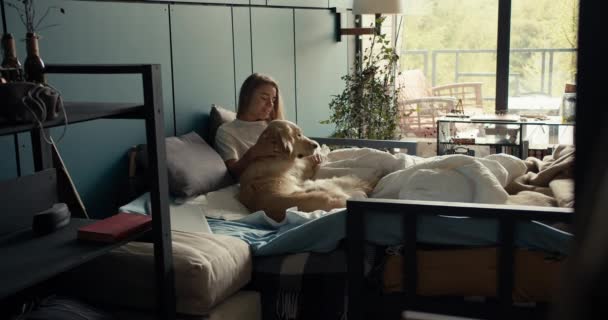 Het Blonde Meisje Ligt Het Bed Met Haar Hond Aait — Stockvideo