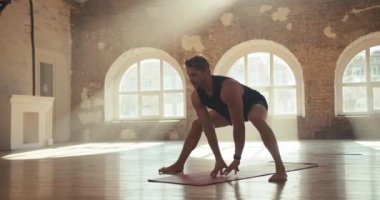 Siyah spor yaz üniformalı bir adamın güneşli bir spor salonundaki özel bir paspasın üzerinde ısınırken ve ısınırken yakın plan fotoğrafı..
