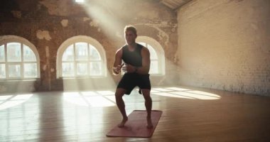 Spor için özel bir halıda güneşli bir spor salonunda egzersiz ve çömelme yapan bir adam. Sabahları güneşli spor salonunda spor yapıyorum..