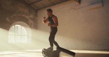 Siyah yaz spor üniformalı bir adam güneşli tuğlalı bir spor salonunda spor yapıyor ve boks yumrukları deniyor..