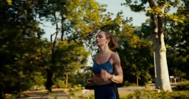 スポーツサマーユニフォームで幸せな女の子の近くのシモンカは 朝の公園を走り 彼女の時計を見ています 記録を達成し 結果を改善する — ストック動画