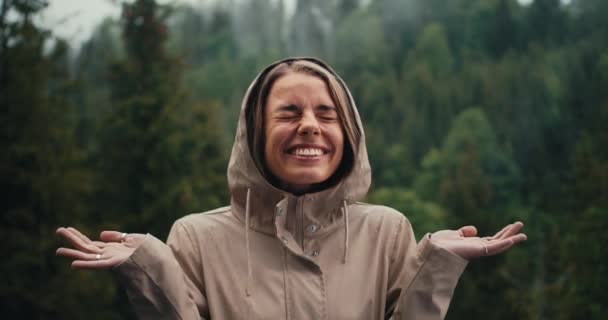 快乐的金发姑娘在森林里的雨中开心地欣赏着高山上的美景和摄像机 — 图库视频影像