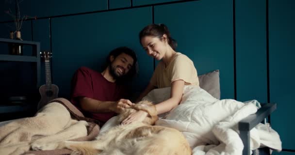 一个穿着红色T恤的黑发男人和一个黑发女孩在家里的绿松石墙的背景下 在床上交流和抚摸着他们的狗 — 图库视频影像