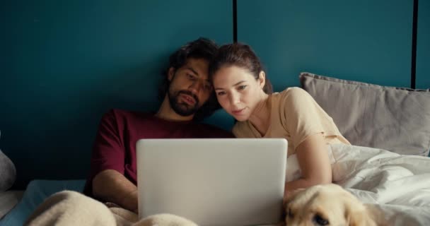 男孩和女孩躺在床上靠着一面碧绿的墙 看着手提电脑的屏幕 这对夫妇共同决定在 — 图库视频影像