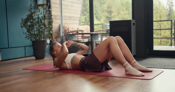 一名身穿白色上衣的金发女孩在一个工业化国家的房子里做运动来锻炼腹部肌肉 家庭健美 — 图库视频影像