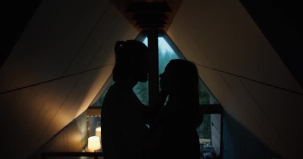 三角屋根のある家で幸せなシルエット 男と女が抱きしめ 暗い部屋で互いに近くに立っています — ストック動画