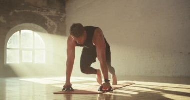 Siyah spor üniformalı bir adam spor yapıyor ve elini Sunny tuğlalı bir salonda özel bir paspasın üzerinde tutuyor..