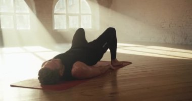 Siyah yaz sporu giymiş bir adam pelvis bölgesini kaldırıyor ve güneşli tuğlalı bir spor salonunda özel bir egzersiz yapıyor..