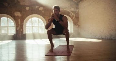 Siyah spor üniformalı bir adam spor yapıyor ve güneşli bir salonda özel bir halıda baldır kasları geliştiriyor..