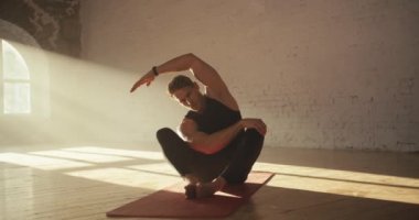 Siyah spor yaz üniforması giyen bir erkek sporcu sırt kaslarını germek için egzersiz yapar. Bir adam kollarını sağa uzatıyor ve geriniyor..