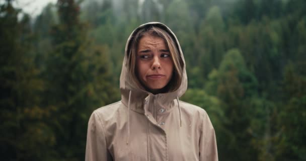 一个悲伤的金发女孩站在山中的森林雨的背景下 她很伤心 看着摄像机 — 图库视频影像