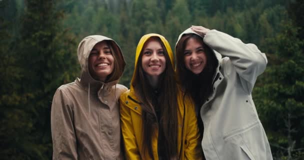 フードの軽いジャケットの3人の少女は 来る雨の中で喜び カメラを見て 山の森で抱擁する — ストック動画