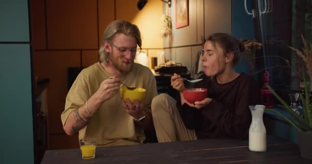 ハッピーカップルガールと男のストレスは朝のキッチンに座って居心地の良い部屋でミルクでシリアルを食べる — ストック動画