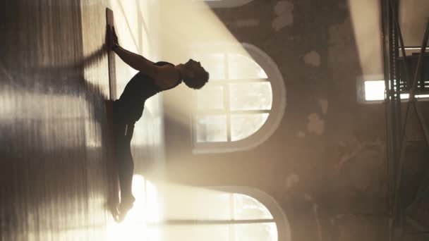 一名身穿黑色运动服的男性运动员在阳光厅做伸展运动和锻炼背部肌肉的垂直录像 — 图库视频影像