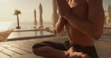 Yakın çekim: Gün doğumunda sahilde meditasyon yapan sakin bir adamın görüntüsü. Açık havada sabah meditasyonu. Beden ve aklın ahengi.