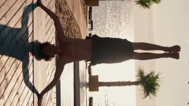 黒いショートパンツのブルネットの男は 朝の晴れたビーチでヨガと瞑想のクラス中に頭の上に立っています — ストック動画