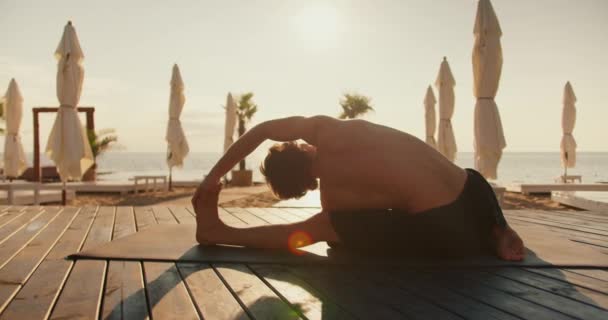 男は午前中に晴れたビーチでストレッチしています 健康のための朝の運動 — ストック動画