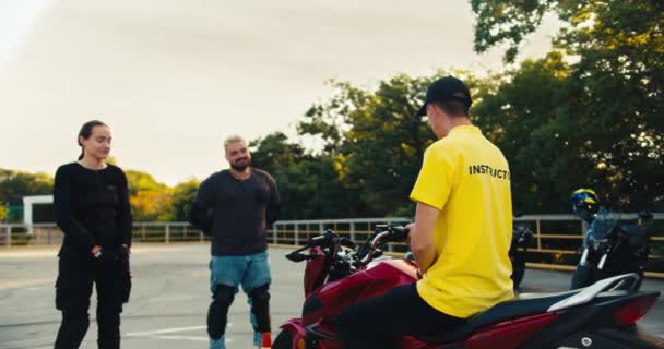 穿着黄色T恤的驾驶教练告诉一个男人和一个女孩如何坐在摩托车上 理论研究后的驾驶练习 — 图库视频影像