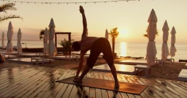 Genç bir adam sabah güneşli bir plajda, güneşin doğuşunda yoga yapar ve vücudunun farklı pozisyonlarını alır. Kerestelerle kaplı güneşli bir sahilde yetişir..