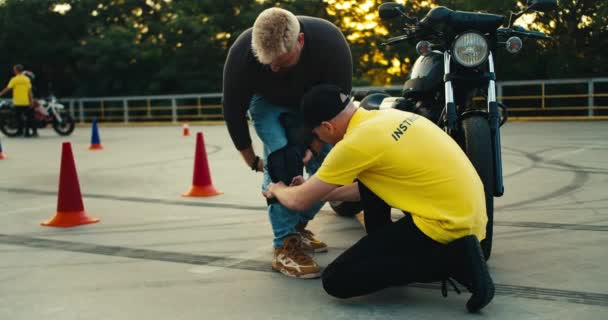 身穿黄色T恤的驾驶教练帮助年轻的自行车手穿上护膝 摩托车和自行车驾驶教官 — 图库视频影像