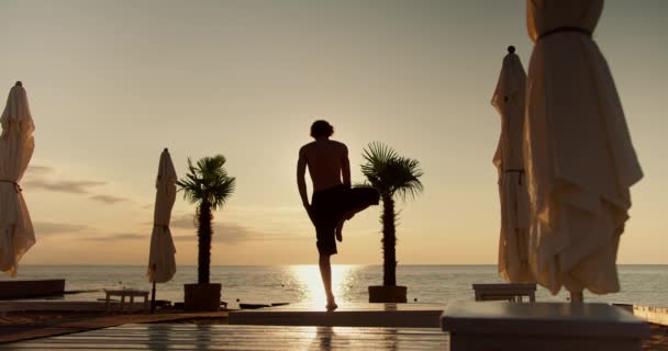 这家伙单腿站立 举起双手 然后在早上把它们放在海滩上 晨曦沉思 — 图库视频影像
