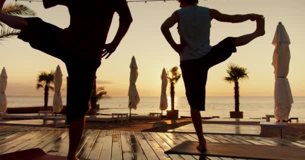 两个人做瑜伽 早上在海滩上单腿站立 日出时的人物形象 — 图库视频影像