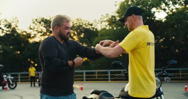 Fahrlehrer Gelben Shirt Hilft Einem Biker Mit Bart Einen Ellbogenschutz — Stockvideo