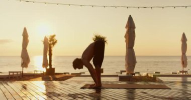 Adam, sabahları güneşli bir sahilde yoga ve meditasyon dersinde ayağa kalkar. Sağlıklı yaşam biçimi, beden ve zihnin uyumu..