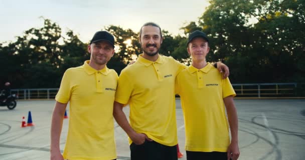 在驾驶学校里 快乐而友善的三位导师 三个穿着黄色T恤的男人在摩托车前摆姿势 — 图库视频影像