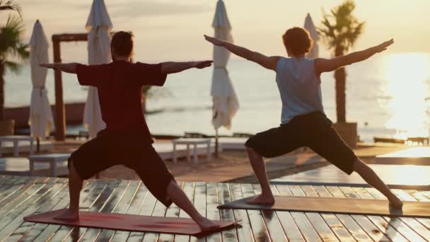 ビーチの木の床に立って 両側に腕を伸ばす2人の男の瞑想 ヨガと禅スタイル — ストック動画