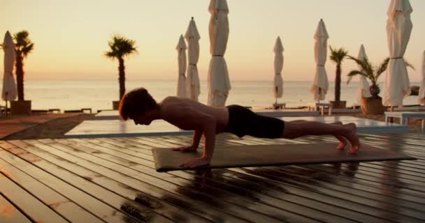 一个赤身裸体的男人早上做瑜伽 在沙滩上铺有木板的特殊垫子上锻炼猫 — 图库视频影像