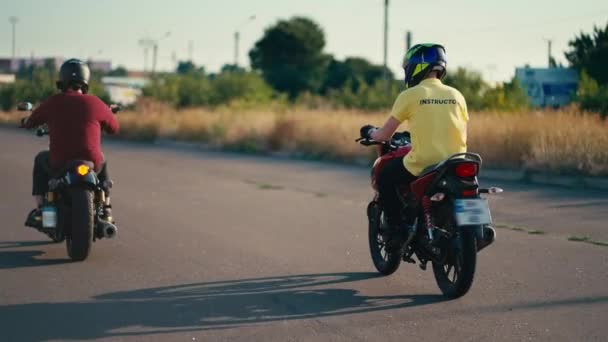 黄色いTシャツとヘルメットのインストラクターが 学生の近くの赤いTシャツとヘルメットでバイクに乗っています ドライビングスクールの学校日 — ストック動画