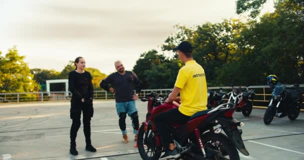 本校快乐的学生和摩托车驾驶教练聊天 一个穿着黄色T恤的男人与一个留着胡子和一个女孩交流 — 图库视频影像