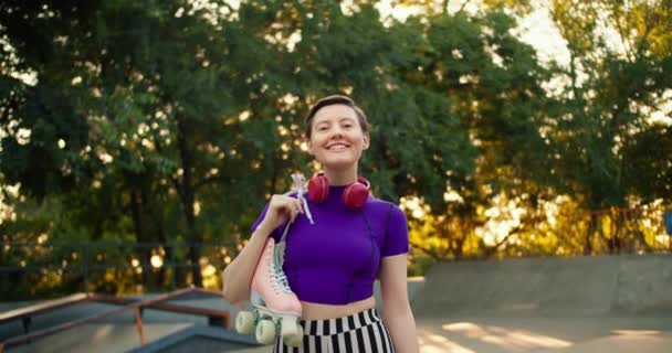 一个身穿紫色上衣 头戴红色耳机的年轻短发女孩的画像 她在一个夏季公园的背景下摆姿势 手里拿着粉红的滚筒 — 图库视频影像