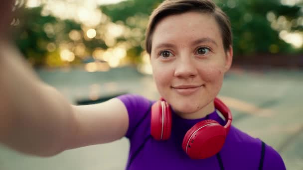 사람보기 헤드폰의 보라색 상단에 머리카락을 소녀는 여름에 스케이트 공원에서 셀카를 — 비디오