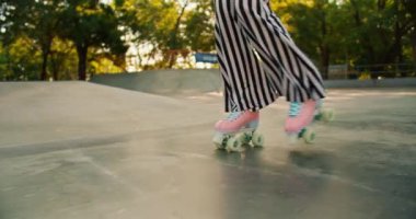 Çizgili pantolon ve pembe paten giyen birinin yaz aylarında kaykay parkında beton zeminde kayarken yakın plan fotoğrafı..