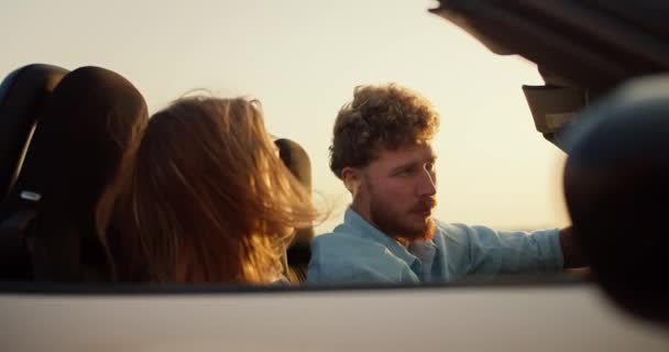 一个留着胡子的家伙 卷曲的头发 穿着蓝色的衬衫 和一个金发姑娘一起开着一辆白色敞篷车 在黄色的天空中飞舞 — 图库视频影像