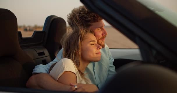一个留着卷发的大胡子男人拥抱着他的金发女友 爱抚着她 外面刮风的时候 一个男的和一个女的坐在一辆敞篷车里 — 图库视频影像
