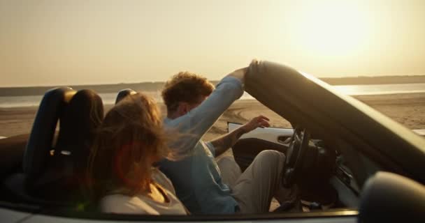 一个留着卷发 穿着蓝色衬衫的大胡子男人坐在一辆白色敞篷车里 旁边坐着一个金发姑娘 在黄天白日的映衬下开车 — 图库视频影像