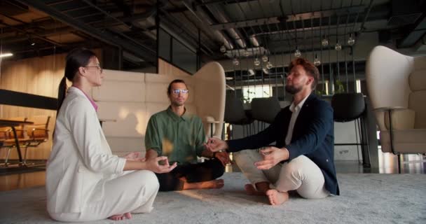 3人のオフィスワーカー 白いスーツの女の子 緑のシャツの男 青いジャケットの男がオフィスのマットで瞑想をしている 職場での瞑想と禅の練習 — ストック動画