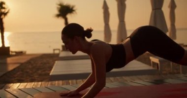 Siyah spor yaz üniformalı esmer bir kızı, yaz mevsiminde Kobra egzersizi yaparken ve yaz aylarında Sunny Plajı 'nda yoga yaparken yakın plan çektim. Altın saat, altın gün doğumu.