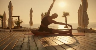 Siyah spor yaz üniformalı bir kız yazın Sunny Beach 'te güneş doğarken kırmızı halıda bacaklarından birine doğru esniyor ve eğiliyor. Güneş ışınlarının parıltısı parıldıyor.