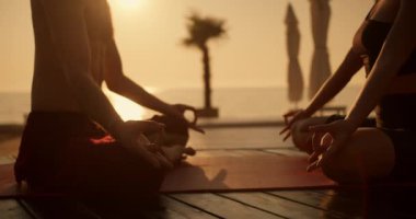 Siyah spor yaz üniformalı bir kız ve siyah şortlu bir adam yaz günbatımında güneşli bir plajda Red Mat 'te meditasyon yaparken yakın çekim..