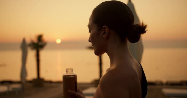 Brunetka Uvázanými Vlasy Pije Ráno Vodu Speciální Láhve Slunné Pláži — Stock video