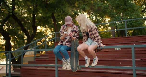 Две Девушки Клетчатых Рубашках Блондинка Брюнетка Кепке Летом Сидят Вместе — стоковое видео
