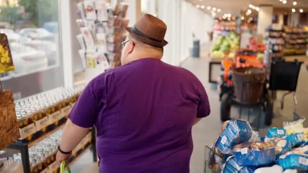 후방보기 보라색 티셔츠와 모자에있는 과체중 남자는 가게를 제품을보고 — 비디오